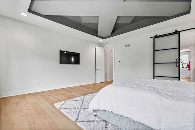 bedroom with a barn door and light hardwood / wood-style floors