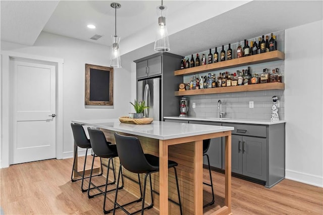 bar with stainless steel refrigerator, gray cabinets, light hardwood / wood-style floors, and hanging light fixtures