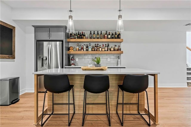 bar featuring decorative light fixtures, light hardwood / wood-style floors, backsplash, gray cabinets, and stainless steel refrigerator with ice dispenser