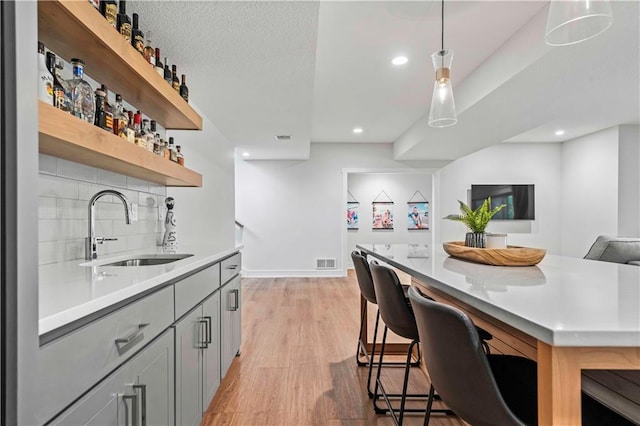 kitchen with light hardwood / wood-style flooring, a breakfast bar, tasteful backsplash, gray cabinetry, and sink