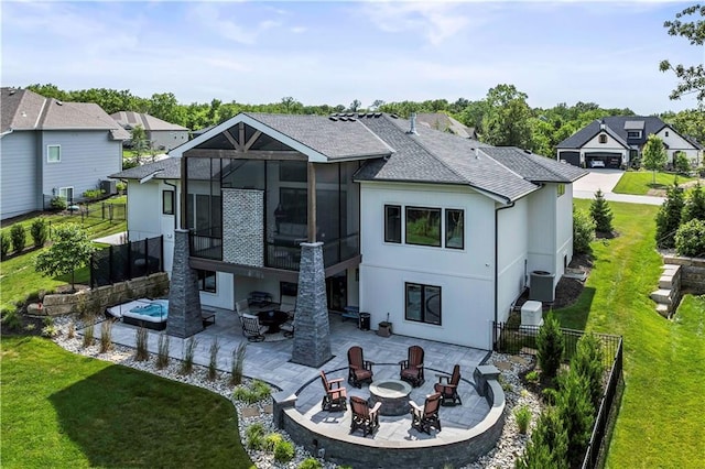 rear view of property with a lawn, glass enclosure, a fire pit, central air condition unit, and a patio area