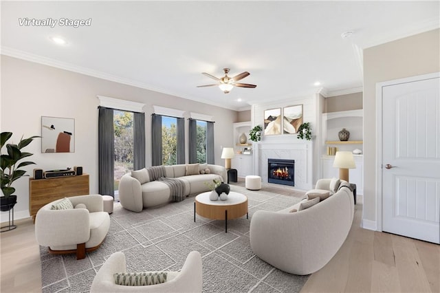 living room with hardwood / wood-style floors, ceiling fan, a high end fireplace, and ornamental molding