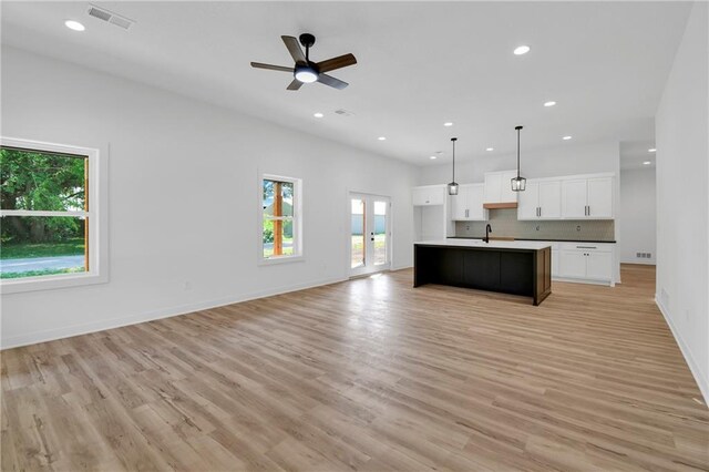 kitchen featuring decorative light fixtures, light wood-type flooring, white cabinetry, an island with sink, and ceiling fan