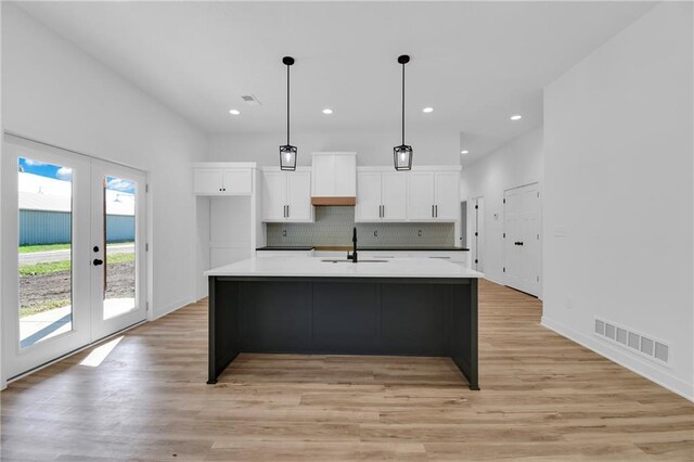 kitchen with sink, light hardwood / wood-style flooring, decorative backsplash, and a center island with sink