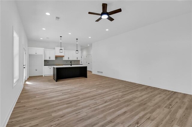 kitchen with ceiling fan, light hardwood / wood-style flooring, hanging light fixtures, white cabinetry, and a center island with sink