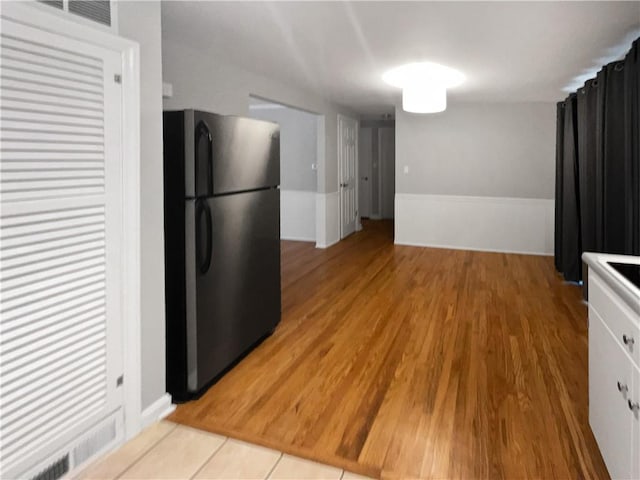 kitchen with white cabinetry, black fridge, and light hardwood / wood-style flooring