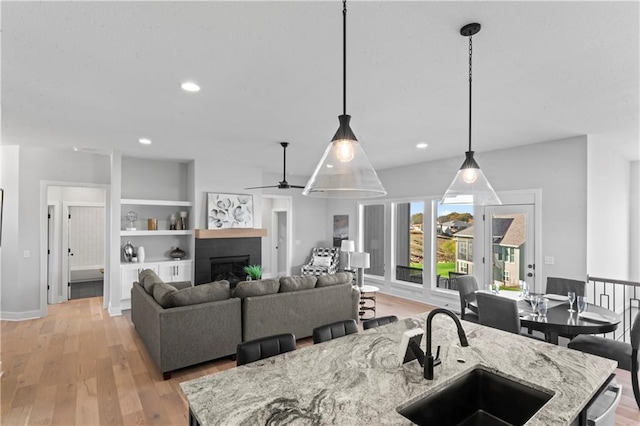 kitchen featuring light stone countertops, hanging light fixtures, sink, and light hardwood / wood-style flooring