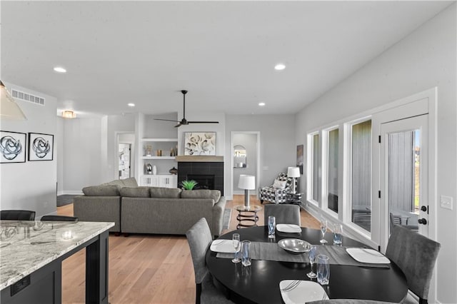 dining space featuring light hardwood / wood-style floors, ceiling fan, and a tile fireplace