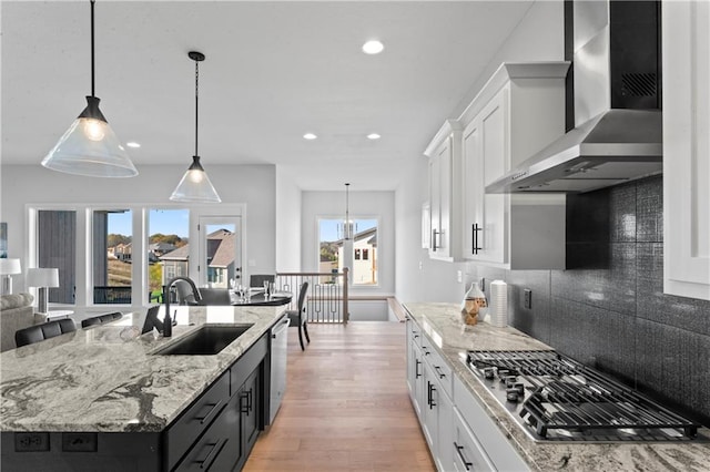 kitchen featuring white cabinetry, wall chimney range hood, appliances with stainless steel finishes, sink, and a kitchen island with sink