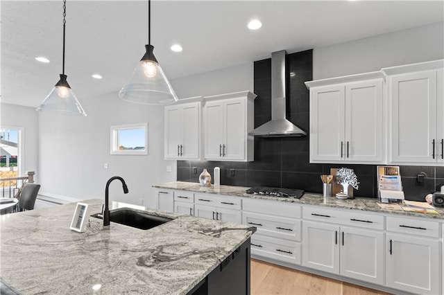 kitchen featuring wall chimney range hood, white cabinets, pendant lighting, sink, and stainless steel gas stovetop