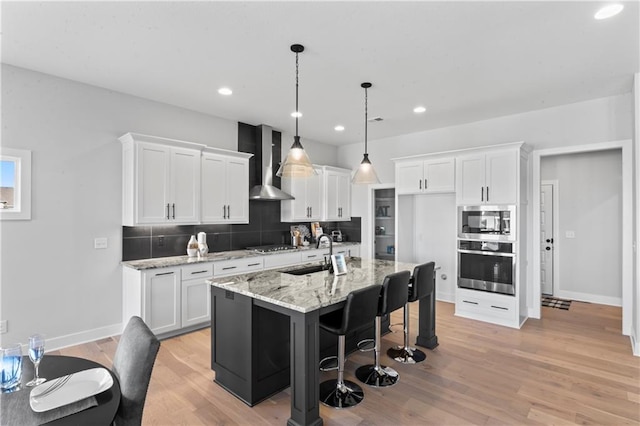 kitchen with white cabinetry, appliances with stainless steel finishes, sink, an island with sink, and wall chimney exhaust hood