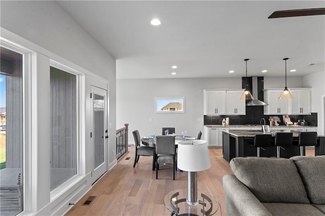 kitchen featuring tasteful backsplash, white cabinetry, pendant lighting, an island with sink, and light hardwood / wood-style floors