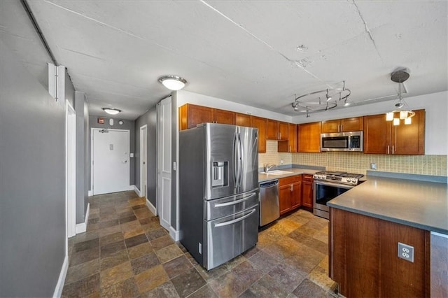 kitchen with sink, tasteful backsplash, track lighting, appliances with stainless steel finishes, and pendant lighting