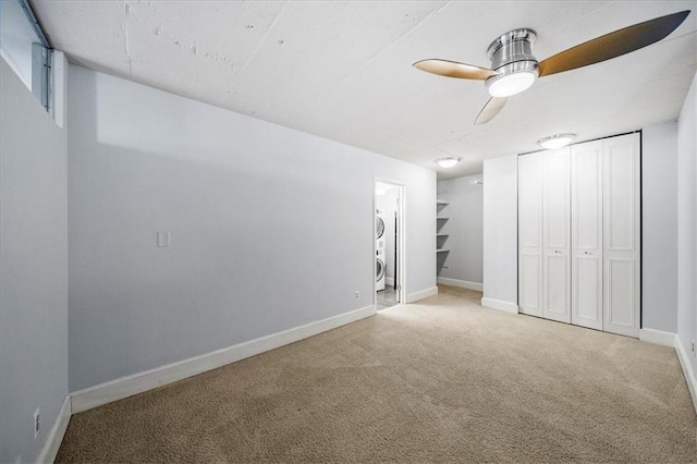 unfurnished bedroom with ensuite bathroom, stacked washer / dryer, light colored carpet, ceiling fan, and a closet