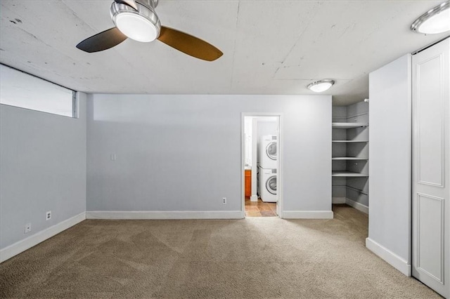 basement featuring stacked washer and clothes dryer, carpet, and ceiling fan