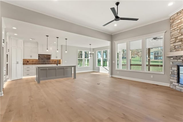 unfurnished living room featuring ceiling fan with notable chandelier, a stone fireplace, sink, light hardwood / wood-style flooring, and ornamental molding