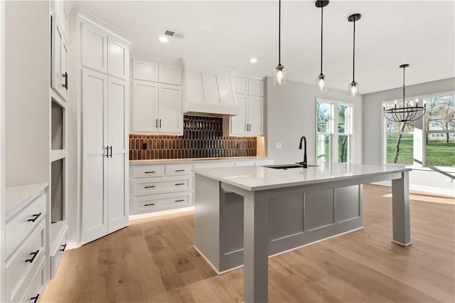 kitchen with white cabinetry, sink, an inviting chandelier, pendant lighting, and a center island with sink