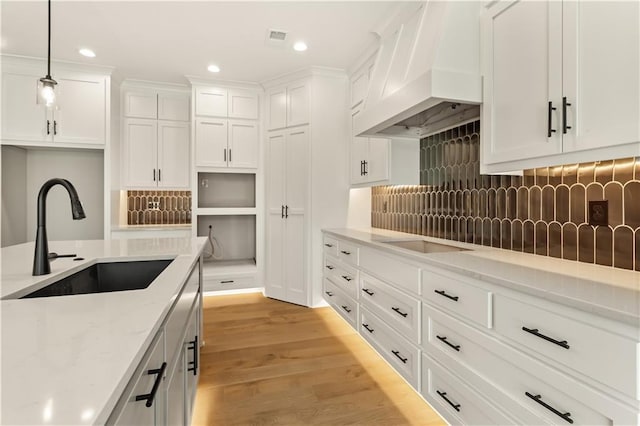 kitchen featuring custom exhaust hood, light wood-type flooring, white cabinetry, and sink