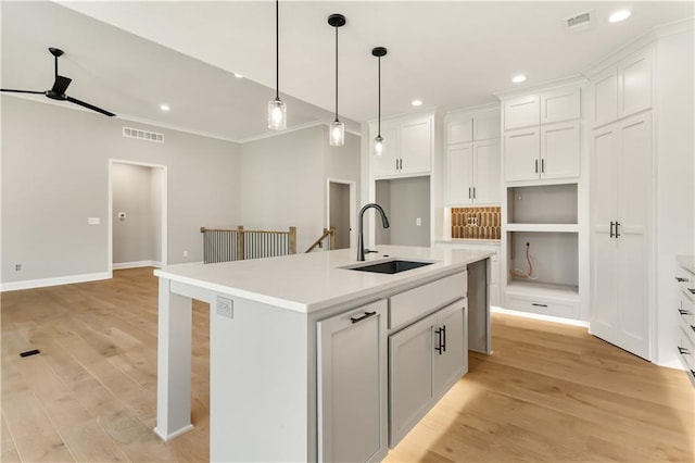 kitchen featuring white cabinetry, sink, ceiling fan, an island with sink, and light wood-type flooring