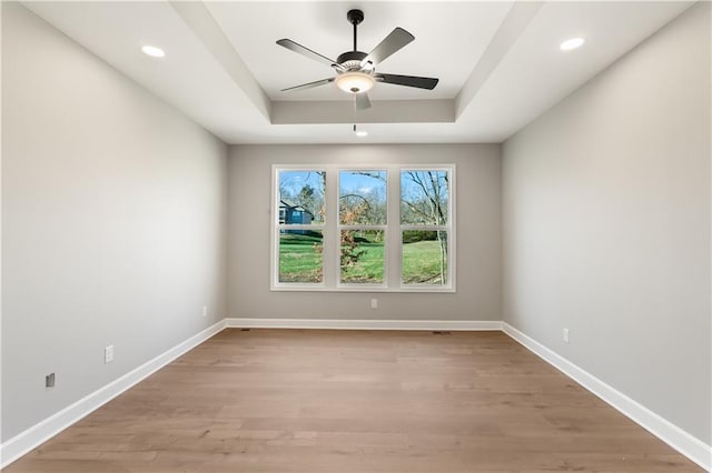 empty room featuring light wood-type flooring, a raised ceiling, and ceiling fan