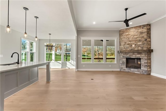 unfurnished living room featuring a stone fireplace, sink, light hardwood / wood-style floors, and plenty of natural light