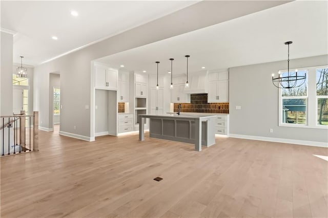 kitchen featuring pendant lighting, a center island with sink, light hardwood / wood-style flooring, a notable chandelier, and white cabinetry