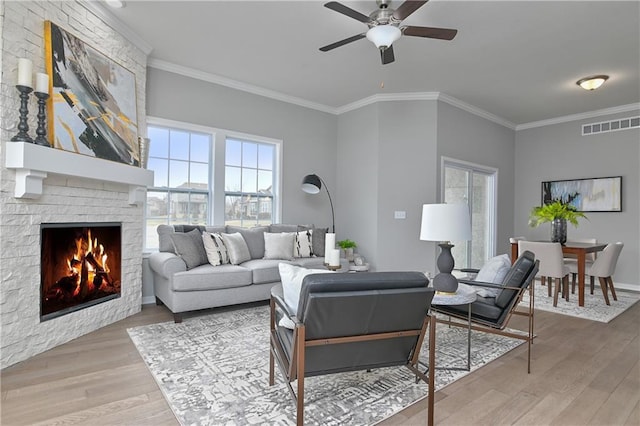 living room featuring wood-type flooring, a stone fireplace, ceiling fan, and crown molding