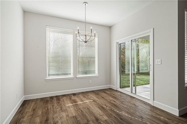 unfurnished dining area with plenty of natural light, dark hardwood / wood-style flooring, and an inviting chandelier