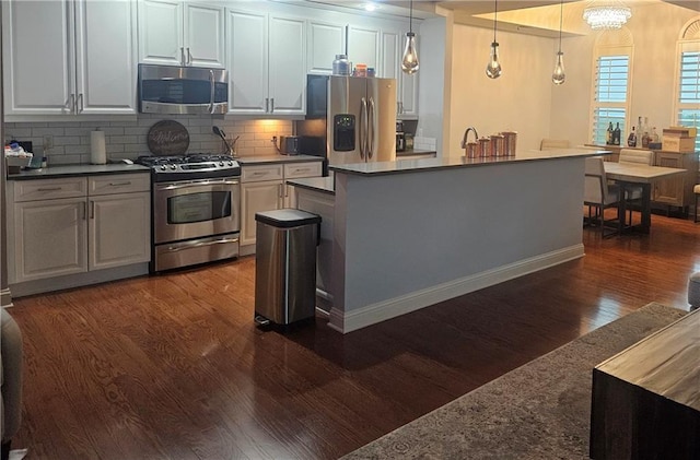 kitchen with tasteful backsplash, pendant lighting, dark wood-type flooring, a notable chandelier, and appliances with stainless steel finishes