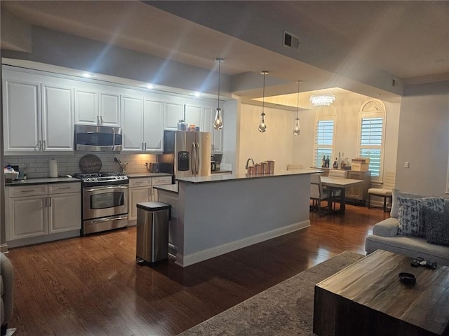 kitchen with appliances with stainless steel finishes, white cabinets, dark hardwood / wood-style floors, decorative light fixtures, and tasteful backsplash