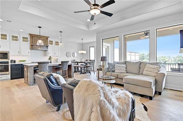 living area with a tray ceiling, crown molding, visible vents, light wood-style floors, and ceiling fan