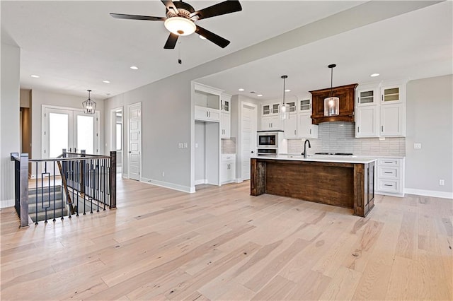 kitchen featuring light wood-type flooring, decorative backsplash, hanging light fixtures, white cabinets, and a center island with sink