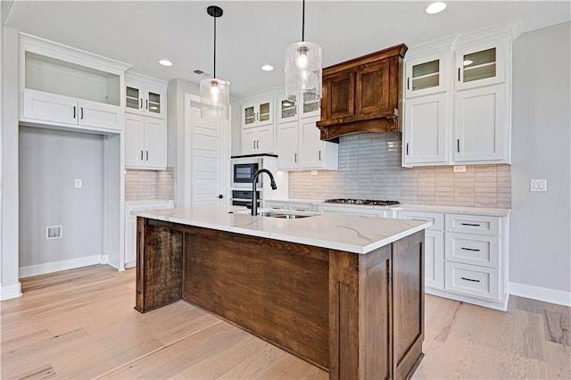 kitchen featuring a sink, white cabinets, built in microwave, light wood finished floors, and a center island with sink