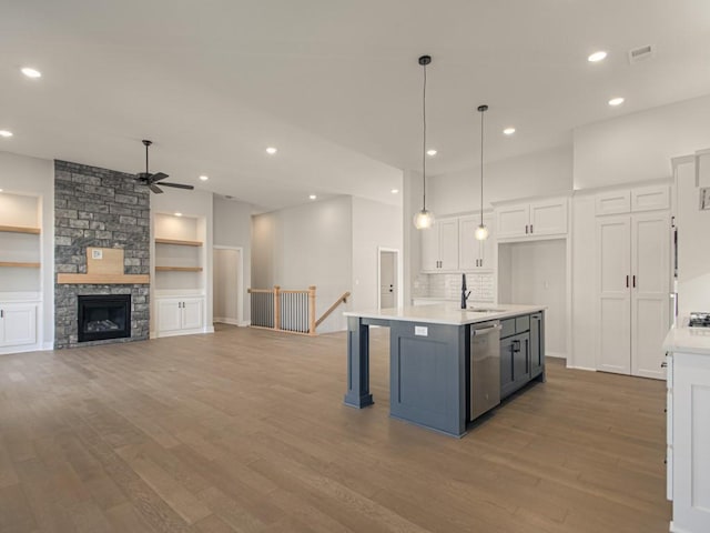 kitchen featuring hanging light fixtures, stainless steel dishwasher, white cabinets, hardwood / wood-style flooring, and a kitchen island with sink