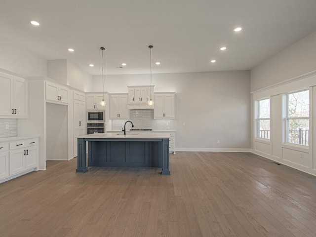 kitchen featuring hanging light fixtures, appliances with stainless steel finishes, a center island with sink, and hardwood / wood-style floors