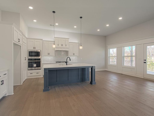 kitchen with appliances with stainless steel finishes, white cabinets, a center island with sink, and wood-type flooring