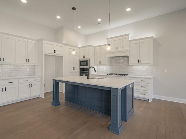 kitchen featuring appliances with stainless steel finishes, dark hardwood / wood-style floors, pendant lighting, white cabinets, and a center island with sink