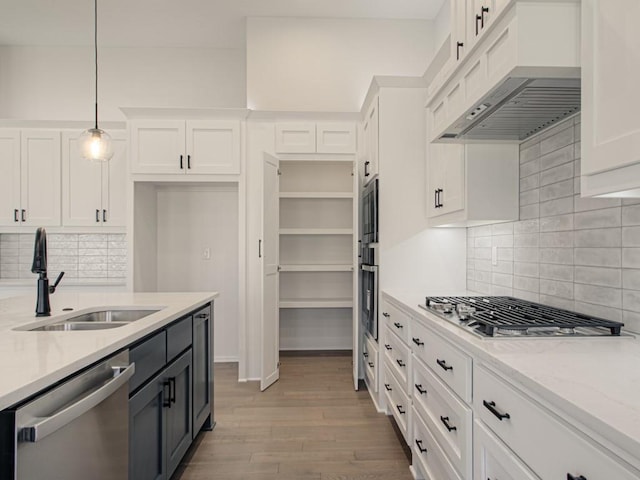 kitchen with white cabinets, appliances with stainless steel finishes, light stone countertops, pendant lighting, and sink