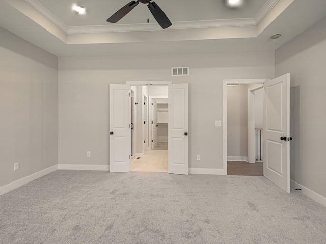 unfurnished bedroom with crown molding, light carpet, a tray ceiling, and ceiling fan