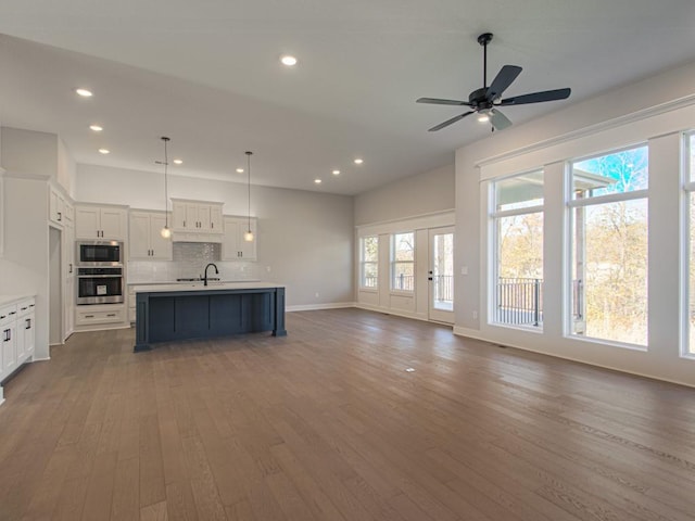 kitchen featuring stainless steel appliances, a center island with sink, hardwood / wood-style floors, decorative light fixtures, and white cabinets