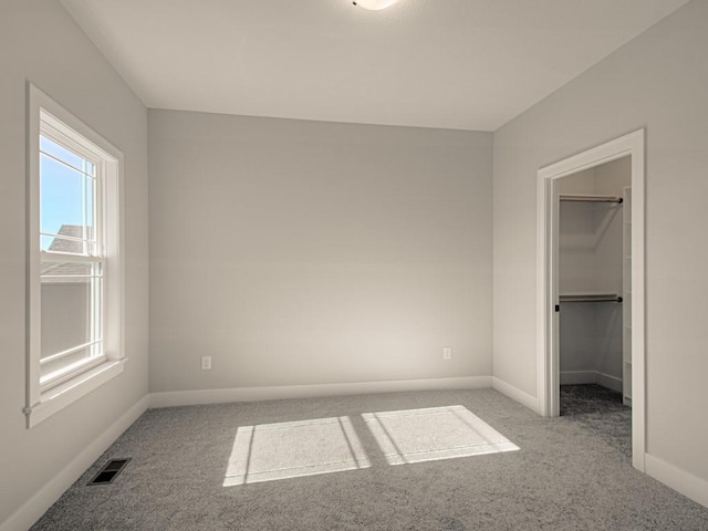 unfurnished bedroom with a spacious closet, light carpet, and a closet