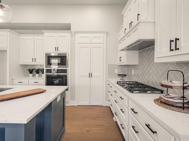 12435 Appaloosa St, Platte City, MO 64079 - kitchen featuring appliances with stainless steel finishes, white cabinetry, wood finished floors, tasteful backsplash, and light stone counters