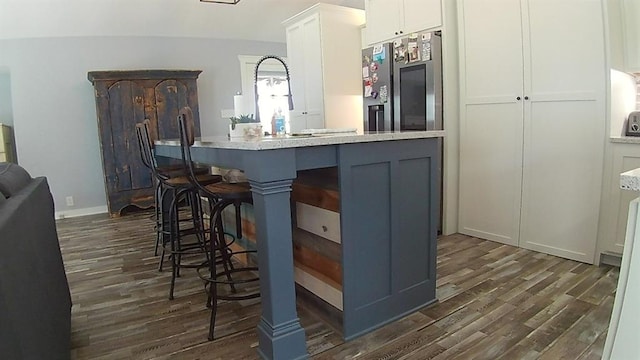 kitchen featuring dark wood-style floors, a sink, white cabinets, a kitchen bar, and stainless steel fridge