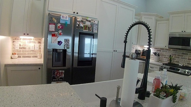 kitchen featuring tasteful backsplash, white cabinets, stainless steel appliances, and light stone counters