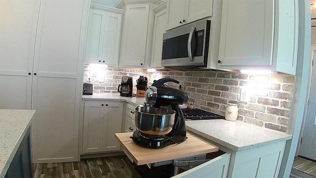 kitchen featuring stainless steel microwave, backsplash, dark wood-style floors, and white cabinetry