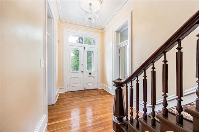 foyer entrance with an inviting chandelier, ornamental molding, and light wood-type flooring