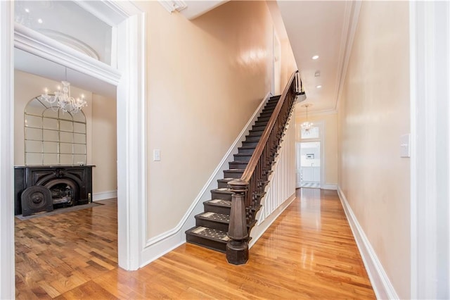 staircase featuring an inviting chandelier, crown molding, and wood-type flooring