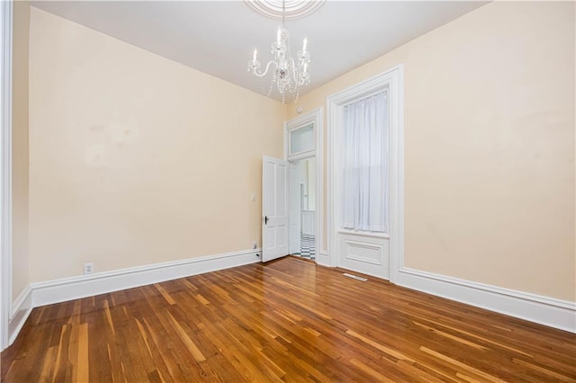 spare room with hardwood / wood-style floors and a notable chandelier