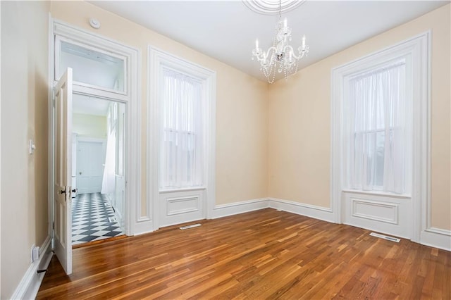 empty room with dark wood-type flooring and an inviting chandelier