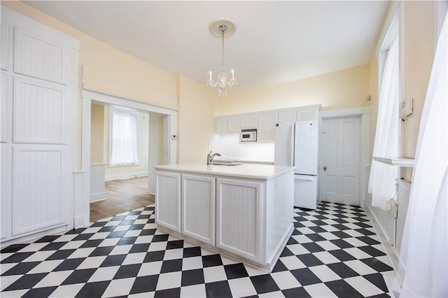 kitchen with white appliances, a kitchen island with sink, white cabinets, decorative light fixtures, and a chandelier